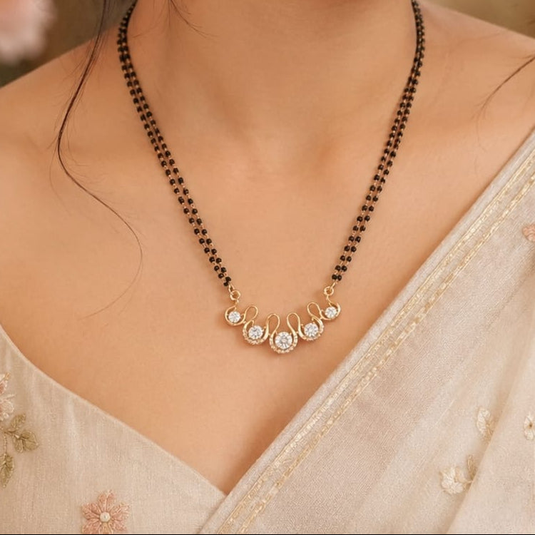 A woman wearing a traditional Indian black bead manjra necklace with a gold-toned pendant featuring small white stones, paired with a light beige floral embroidered saree.