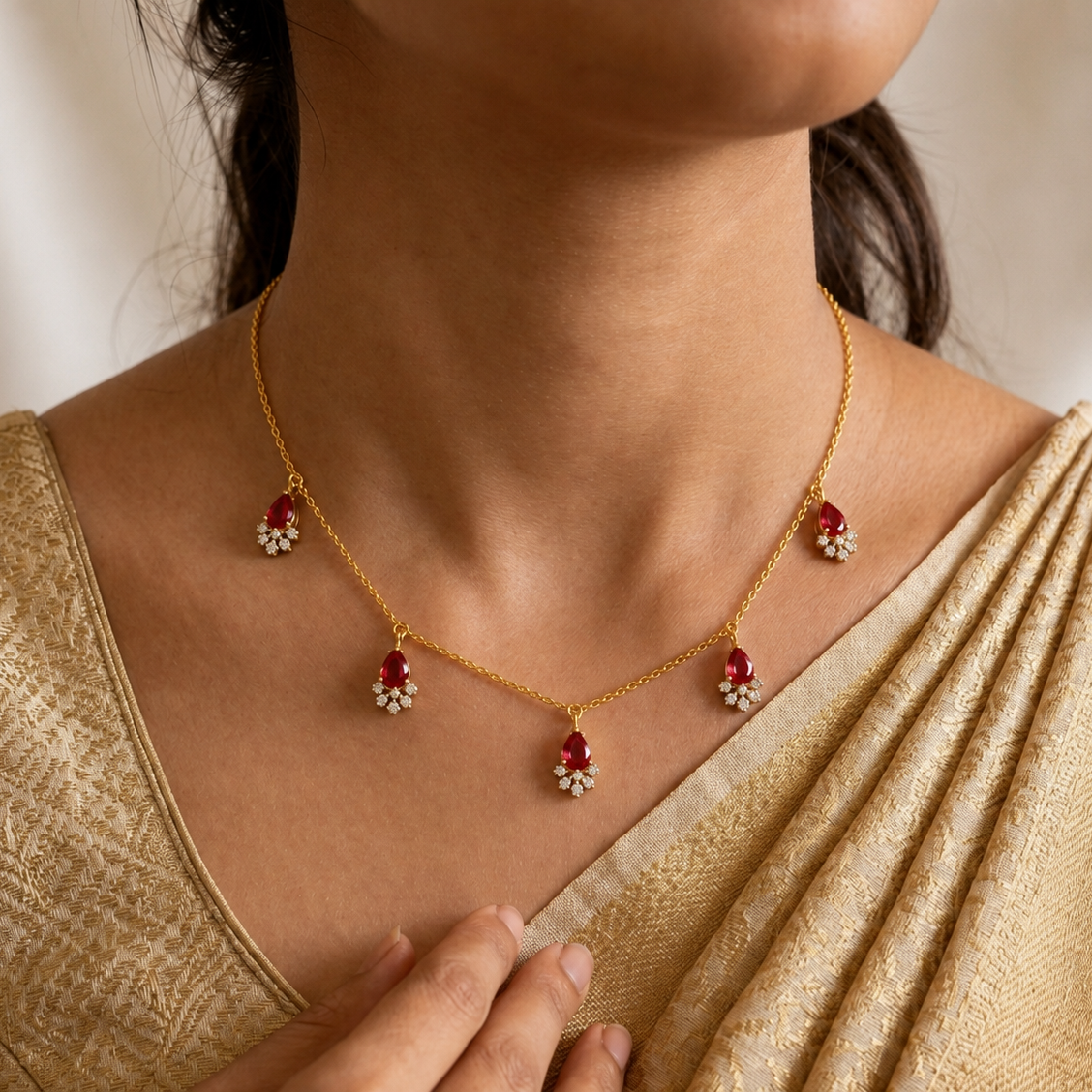 A close-up of a woman wearing a gold necklace with five red and white floral-shaped pendant clusters, paired with a gold saree.